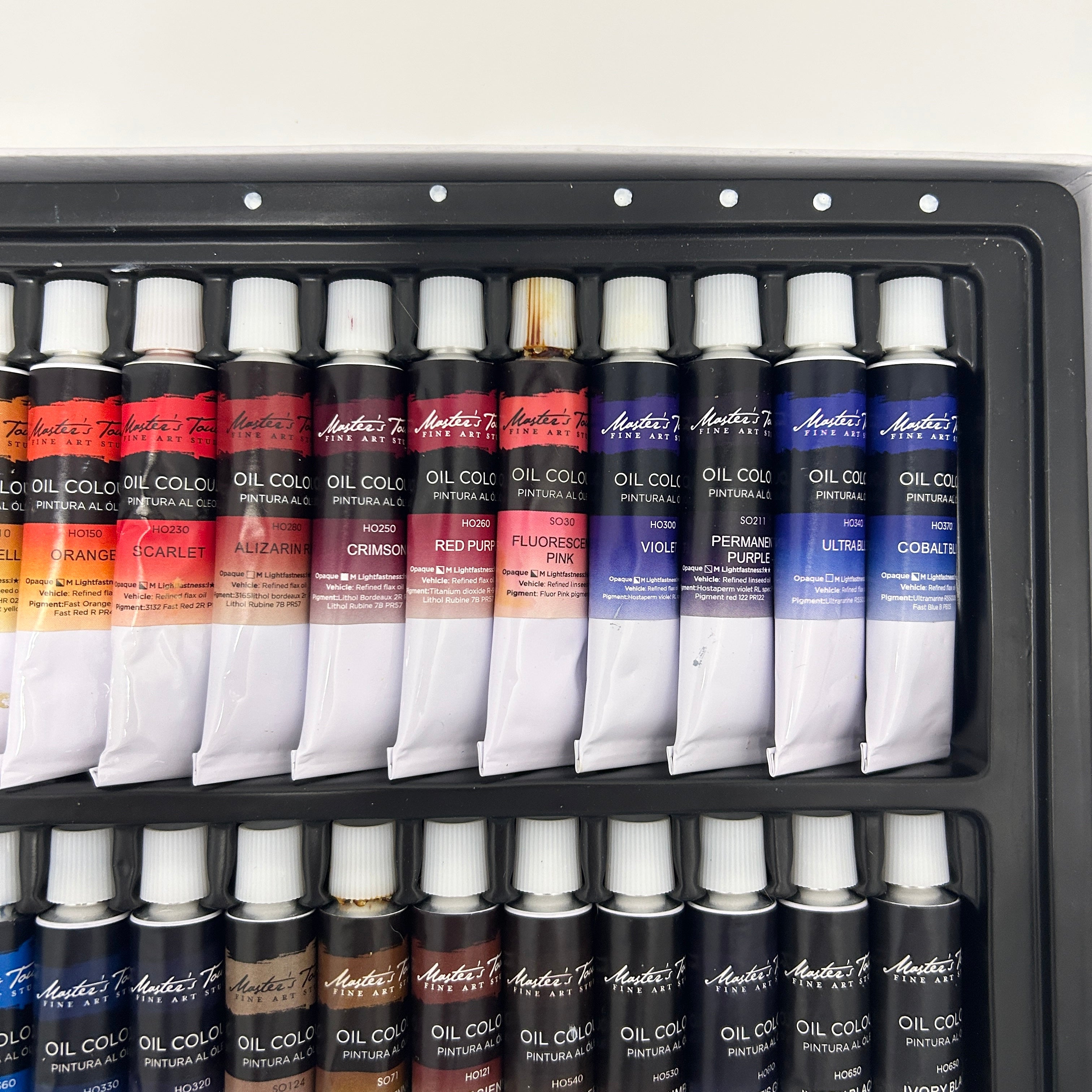 Set of oil paint tubes in a black tray on a white background