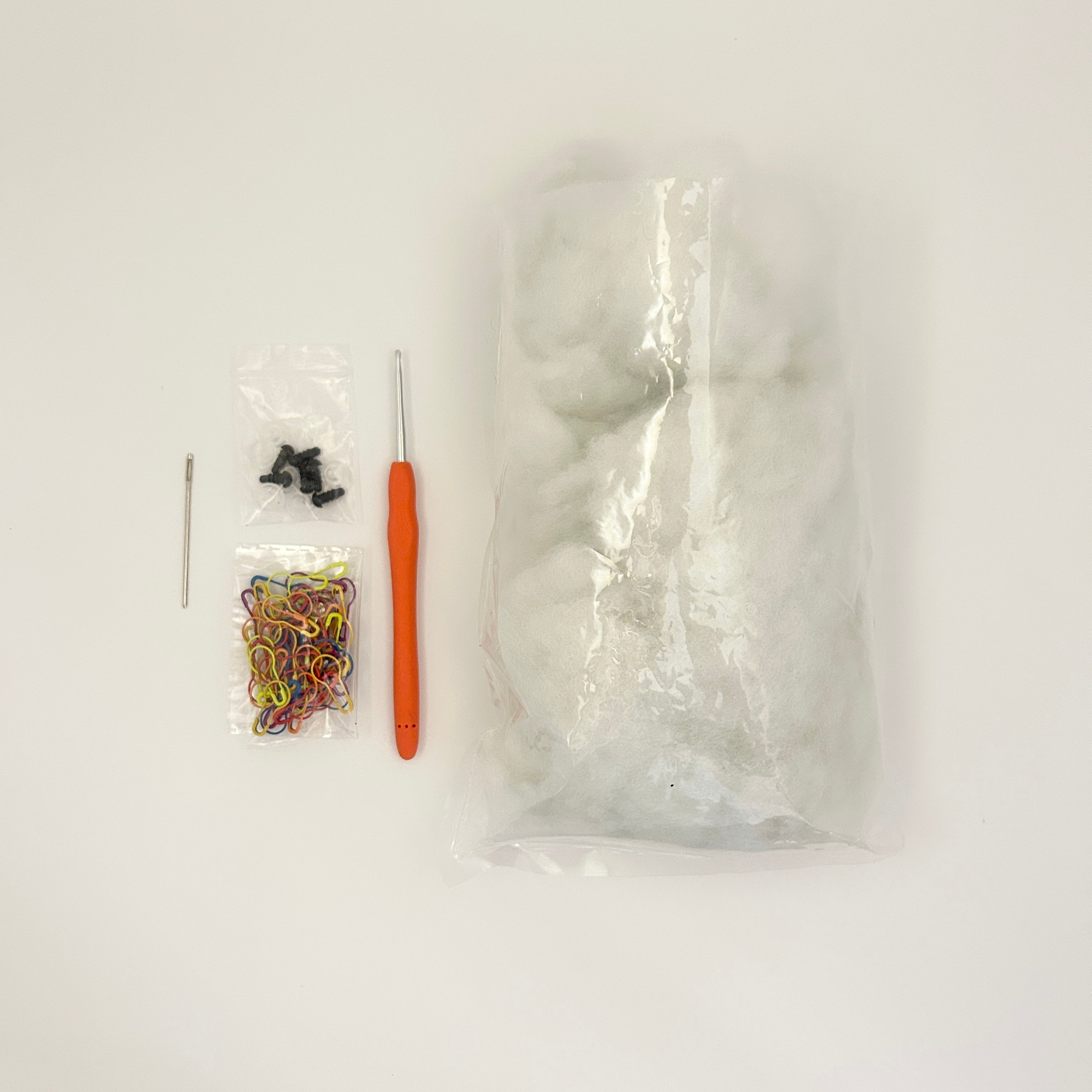 Craft supplies including a crochet hook, rubber bands, and a clear plastic bag on a white background